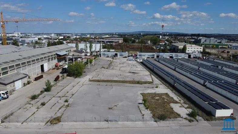 Luftaufnahme eines Industriegebiets mit großen Hallen, einem weitläufigen Betonplatz und Solaranlagen.