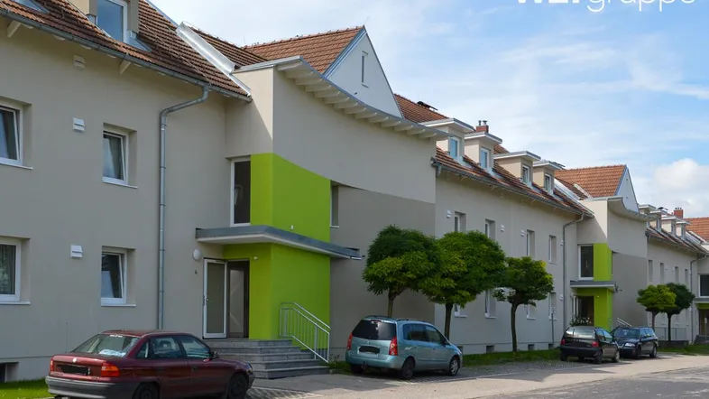 Reihenhäuser mit moderner Fassadengestaltung und Parkplätzen vor dem Gebäude unter blauem Himmel.