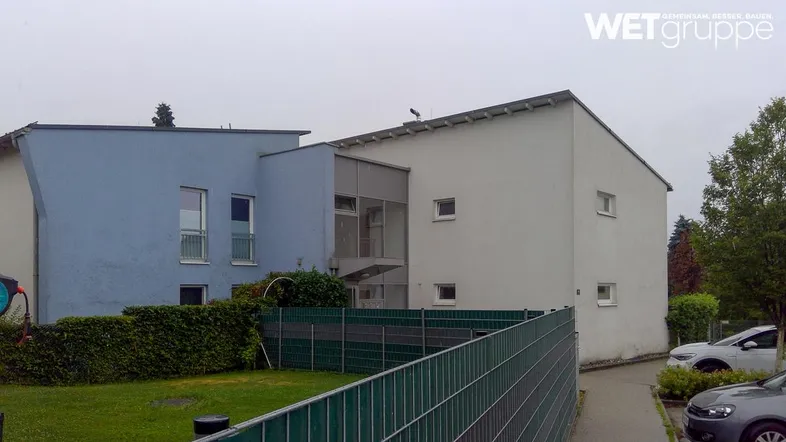 Modernes Gebäude mit blauer und weißer Fassade, umgeben von Grünflächen und einem Zaun.