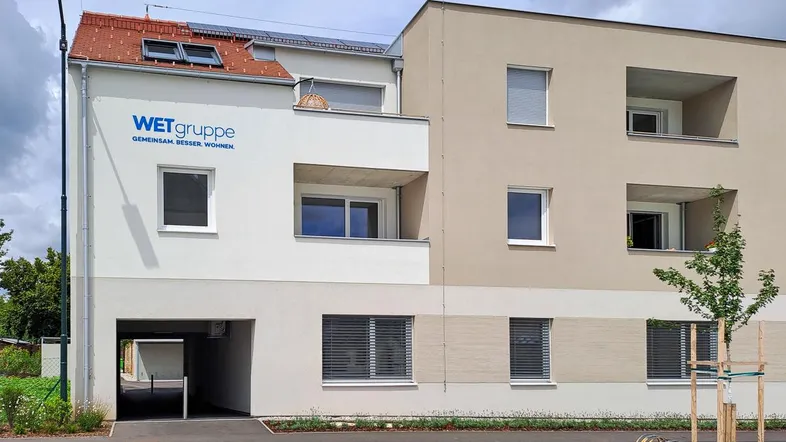 Modernes Mehrfamilienhaus mit heller Fassade, Balkonen und Photovoltaikanlage auf dem Dach.