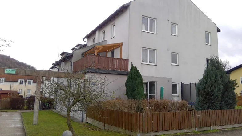 Mehrfamilienhaus mit heller Fassade, Balkon und kleinem Vorgartenbereich.