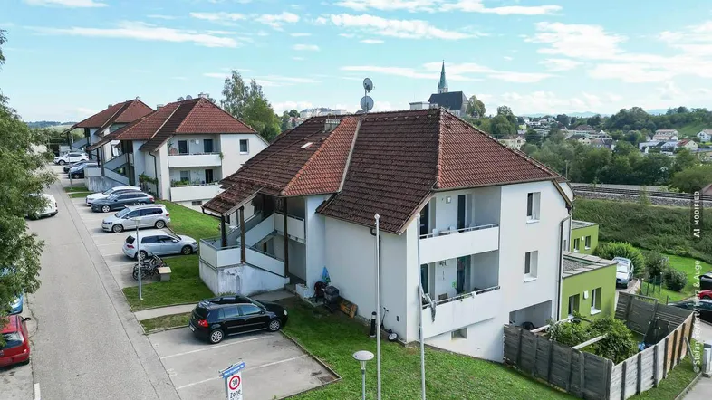 Luftaufnahme eines Wohngebäudes mit Satteldach, Parkplätzen und Blick auf die Umgebung.