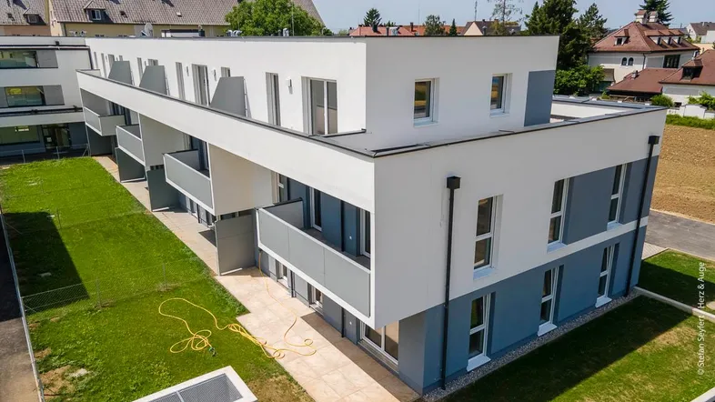 Modernes Mehrfamilienhaus mit weißer und grauer Fassade, Balkonen und gepflegten Grünflächen.
