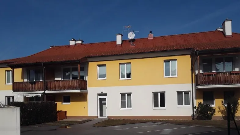 Gelbes und weißes Gebäude mit roten Ziegeldächern und Holzbalkonen unter blauem Himmel.