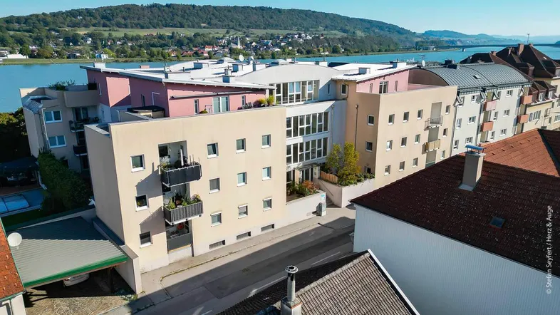 Moderne Wohnanlage mit mehreren Gebäuden, Balkonen und Blick auf den See und die umliegende Landschaft.
