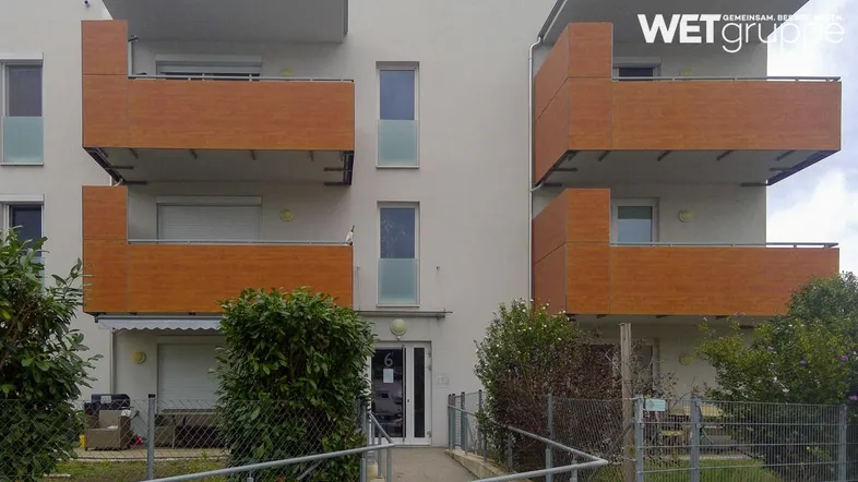 Moderne Wohnanlage mit hellen Fassaden und Balkonen mit Holzverkleidung, inklusive barrierefreiem Zugang.