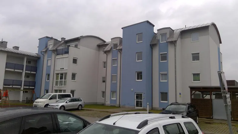 Mehrfamilienhaus mit moderner Fassade in Blau und Grau, umgeben von Parkplätzen.