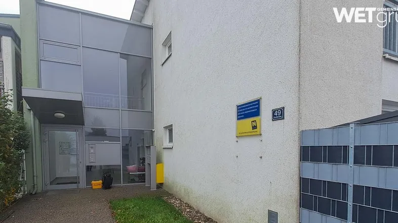Außenansicht eines modernen Gebäudes mit heller Fassade und gläsernem Eingangsbereich.