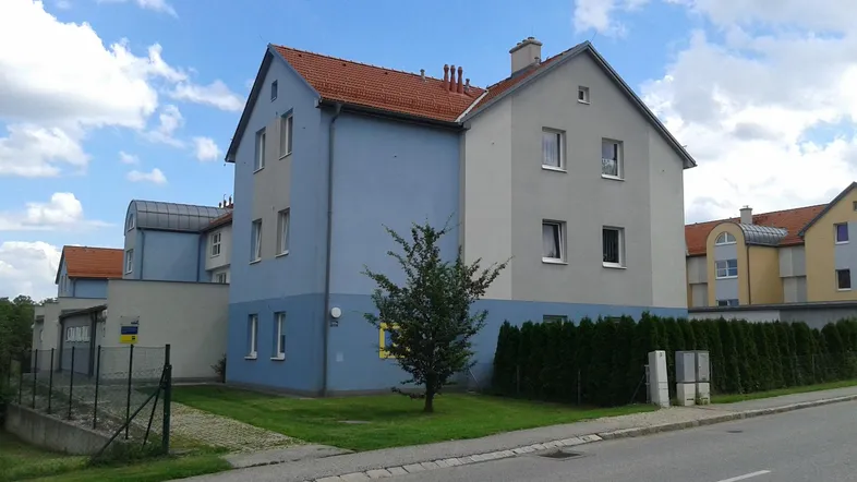 Modernes Mehrfamilienhaus mit blauer und grauer Fassade unter einem Satteldach in grüner Umgebung.