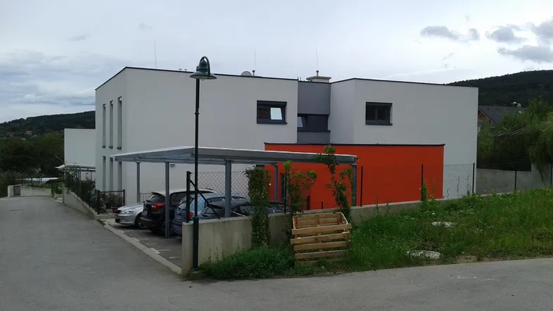 Moderne Wohnanlage mit weißer und oranger Fassade, Flachdach und Carport in ländlicher Umgebung.
