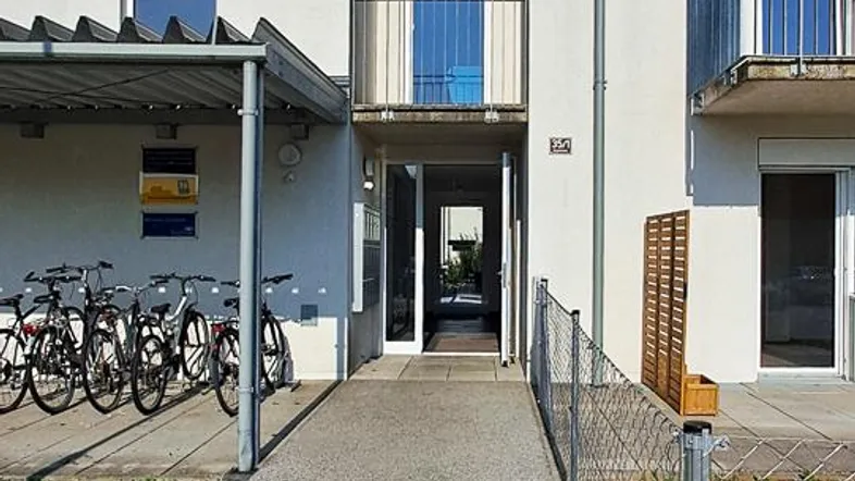 Moderner Eingangsbereich eines Mehrfamilienhauses mit Fahrradabstellplatz und gepflegtem Gehweg.