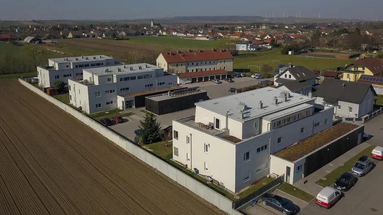 Luftaufnahme von modernen Wohngebäuden mit Flachdächern in ländlicher Umgebung und weitem Blick über Felder.