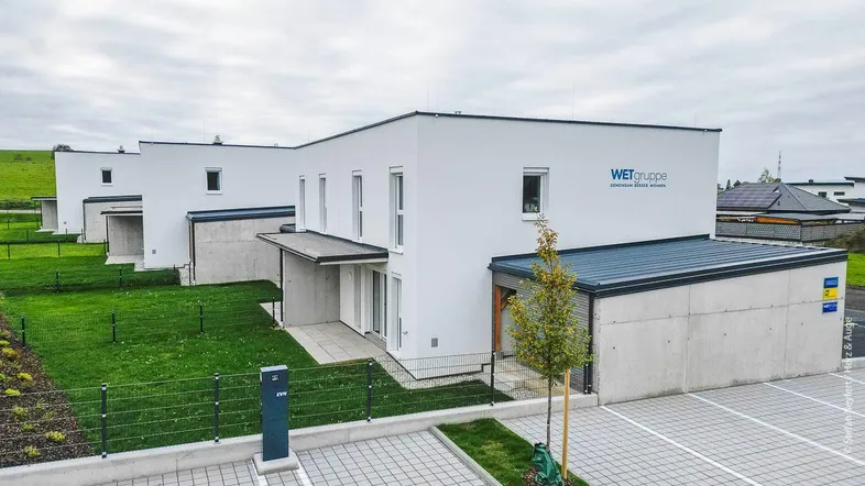Moderne Reihenhäuser mit weißen Fassaden, gepflegten Rasenflächen und gepflasterten Parkplätzen.