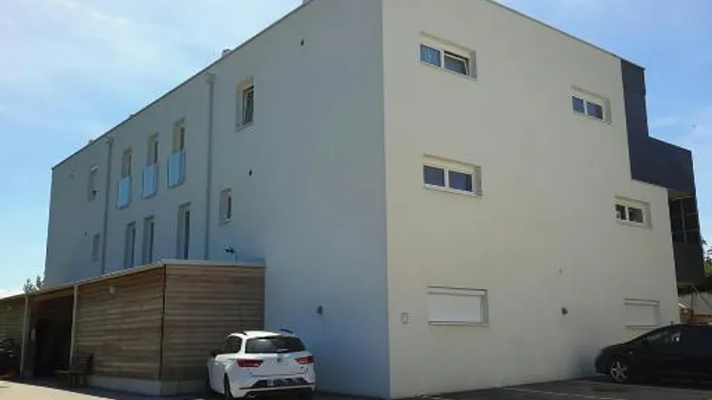 Modernes Mehrfamilienhaus mit heller Fassade, Balkonen und Außenparkplätzen.