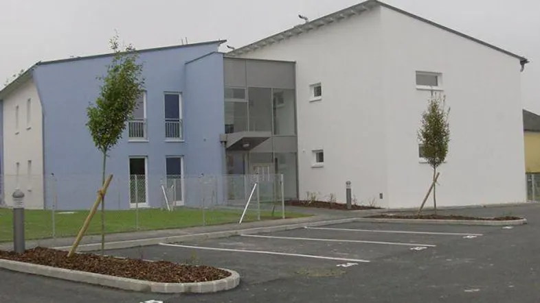 Modernes Gebäude mit blauer und weißer Fassade, großen Glasflächen und zugehörigen Parkplätzen.