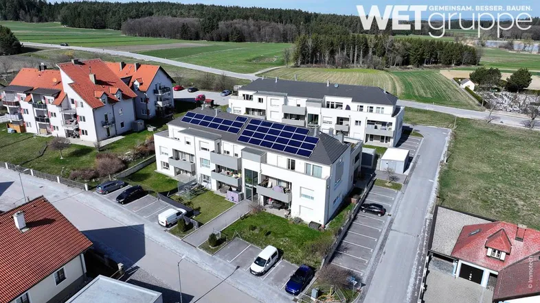 Luftaufnahme von modernen Wohngebäuden mit Photovoltaikanlagen und grüner Umgebung.