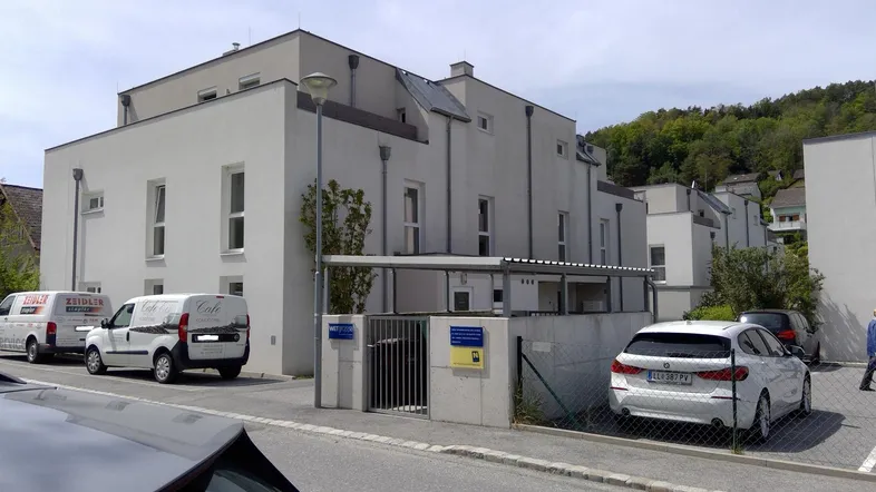 Modernes Mehrfamilienhaus mit weißer Fassade, großen Fenstern und Tiefgaragenzufahrt, umgeben von Grün.