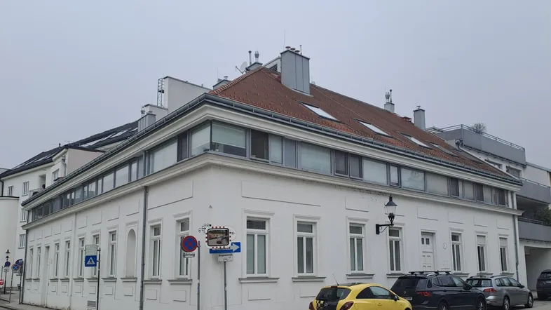 Weißes Eckgebäude mit klassischer Architektur und modernen Dachfenstern an einer Stadtstraße.