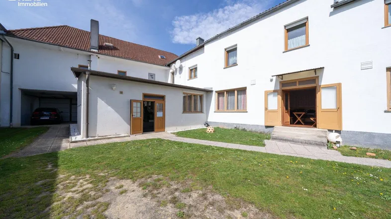 Außenansicht des Gebäudes mit weißer Fassade, kleinem Rasenbereich und Carport.