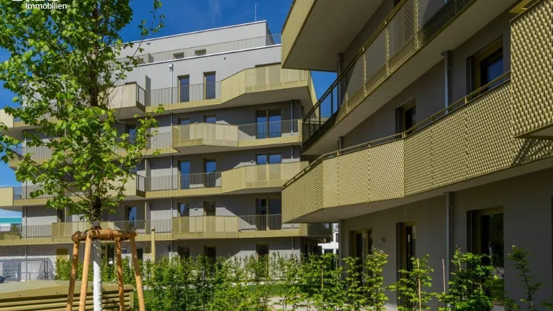 Moderne Wohnanlage mit mehreren Etagen, Balkonen und begrünten Außenbereichen unter blauem Himmel.