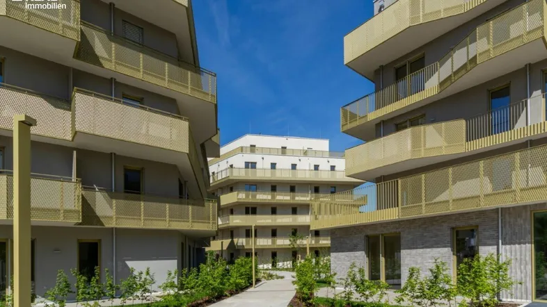 Moderne Wohngebäude mit goldfarbenen Balkonen und gepflegten Grünflächen unter blauem Himmel.