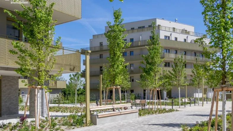 Moderne Wohngebäude mit ansprechend gestalteten Außenanlagen, Gehwegen und jungen Bäumen unter blauem Himmel.