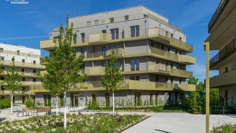 Moderne Wohngebäude mit Balkonen und begrünten Außenanlagen unter blauem Himmel.