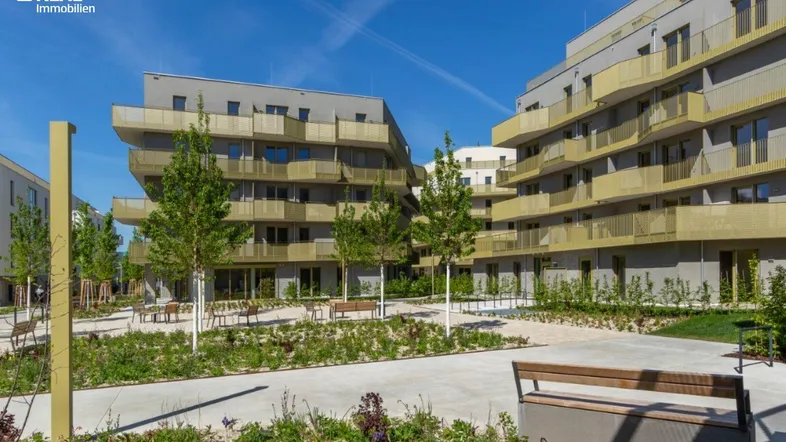 Moderne Wohngebäude mit Balkonen und begrüntem Innenhof unter blauem Himmel.