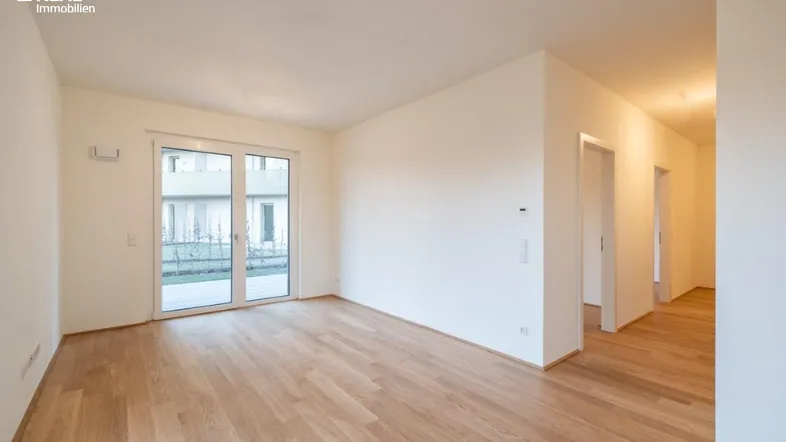 Helles, leeres Zimmer mit Holzboden und Zugang zu einem privaten Gartenbereich.