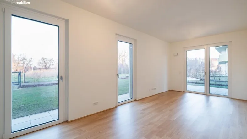 Heller Wohnraum mit Holzboden und großen Fenstertüren, die Zugang zum Garten bieten.