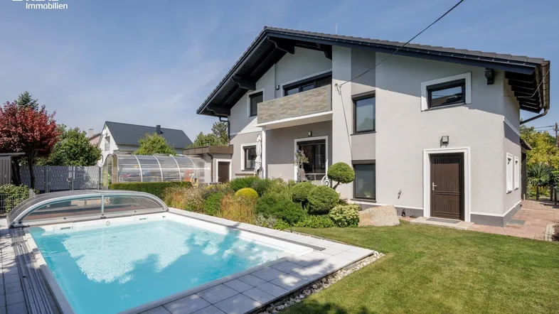 Modernes Haus mit gepflegtem Garten, Swimmingpool und Poolabdeckung unter blauem Himmel.