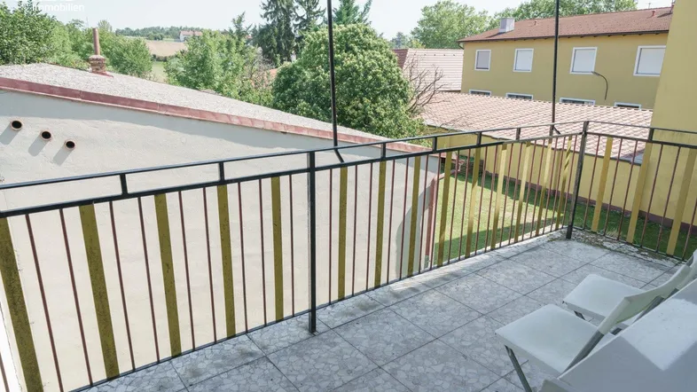 Balkon mit Fliesenboden und Metallgeländer, bietet Blick auf die umliegenden Gebäude und Grünflächen.