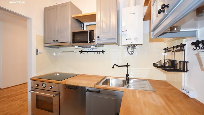 Moderne Küche mit grauen Schränken, Holzarbeitsplatten, integrierten Geräten und einem Boiler an der Wand.