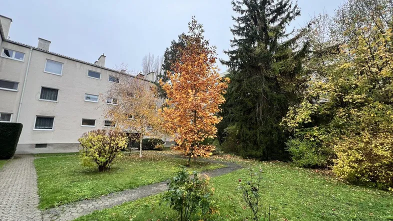 Die Fassade des Gebäudes umgeben von herbstlicher Vegetation und einem gepflegten Rasenbereich.