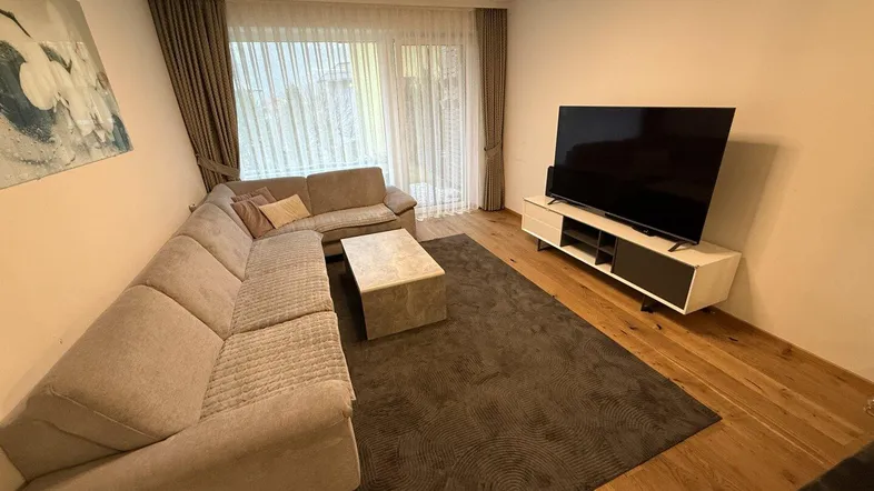 Helles Wohnzimmer mit großem Ecksofa, Holzboden und Zugang zur Terrasse.