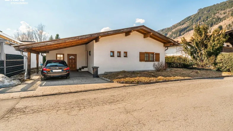Einfamilienhaus mit Carport und Auffahrt, umgeben von einer bergigen Landschaft.