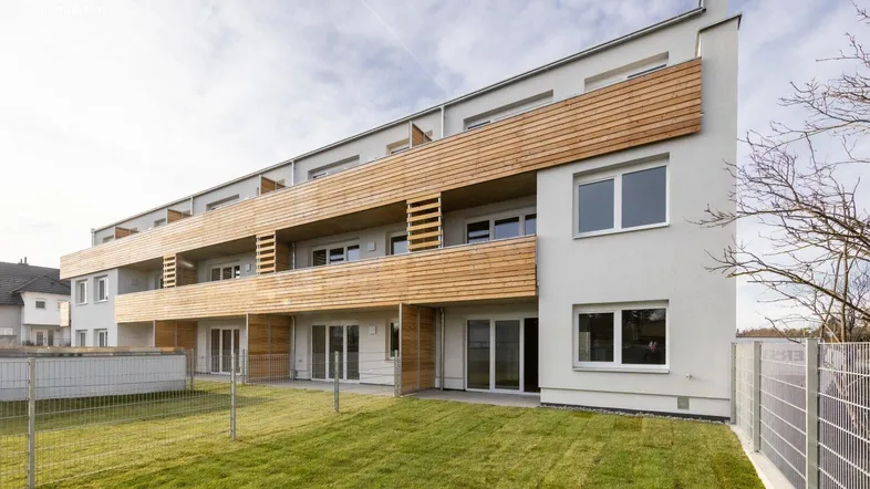 Moderne Wohnanlage mit heller Fassade, Holzverkleidungen an Balkonen und grüner Rasenfläche.