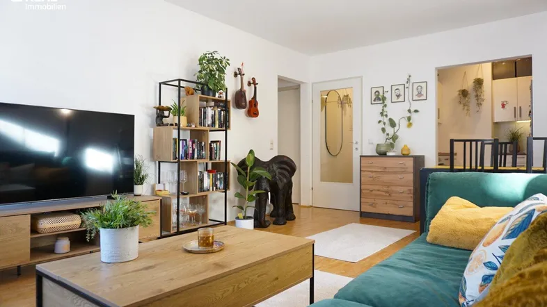 Helles Wohnzimmer mit modernem Regal, Holzboden und offenem Übergang zum Essbereich.