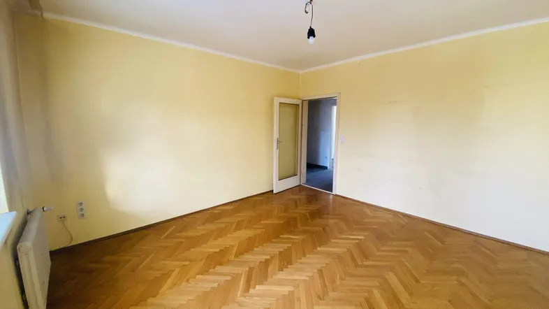 Heller Raum mit Fischgrätparkettboden und gelben Wänden, mit Zugang zu einem weiteren Zimmer.