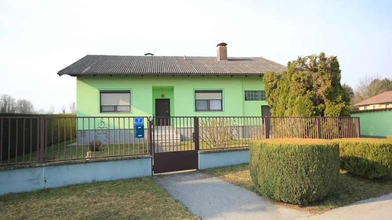Vorderansicht des Einfamilienhauses mit hellgrüner Fassade, Zaun und gepflegtem Vorgarten.