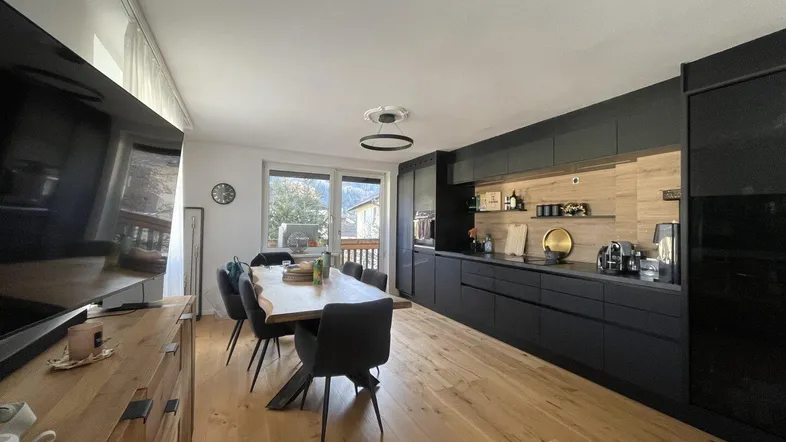 Moderne offene Küche mit schwarzer Front, Holzboden und Essbereich, mit Zugang zu einem Balkon.