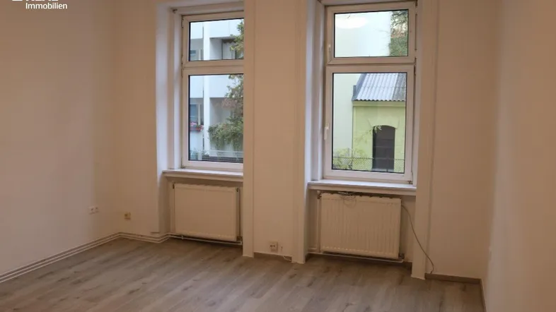 Helles Zimmer mit zwei großen Fenstern, Heizkörpern und neuem Laminatboden.