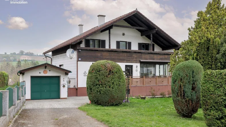 Traditionelles Einfamilienhaus mit Satteldach, Holzverkleidung und Balkon im ländlichen Stil.