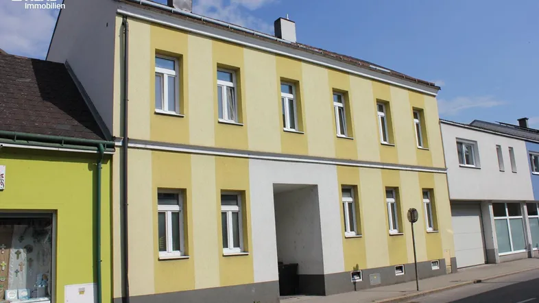Fassade eines Mehrfamilienhauses mit gelb-weiß gestreiften Wänden und einem Durchgang im Erdgeschoss.