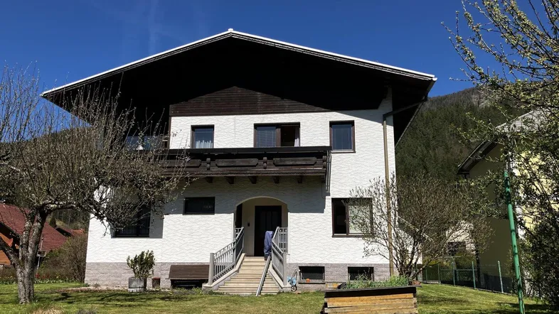 Vorderansicht eines Einfamilienhauses mit weißer Fassade und gepflegtem Vorgarten unter blauem Himmel.