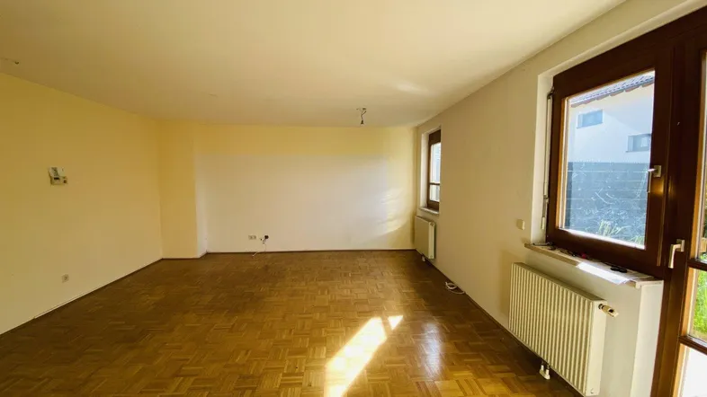 Helles Wohnzimmer mit Parkettboden und großen Fenstern, die viel Tageslicht hereinlassen.