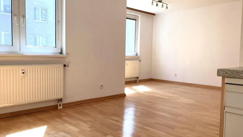 Heller Wohnbereich mit Parkettboden, weißen Wänden und großen Fenstern, der viel Tageslicht bietet.