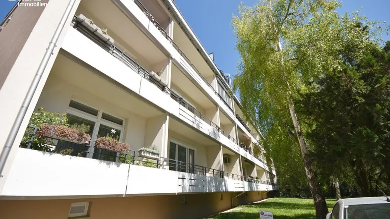Mehrstöckiges Wohngebäude mit mehreren Balkonen und grüner Umgebung unter blauem Himmel.