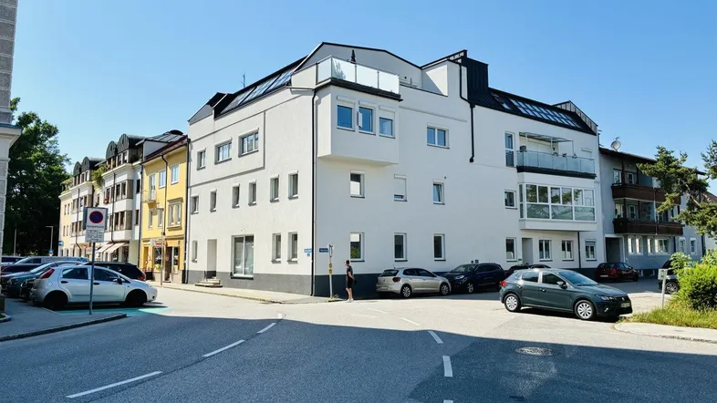 Modernes Mehrfamilienhaus mit weißer Fassade, großen Fenstern und mehreren Balkonen in städtischer Umgebung.