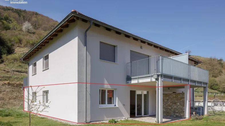 Modernes Einfamilienhaus mit Balkon und Terrasse, umgeben von grüner Natur und Hügellandschaft.